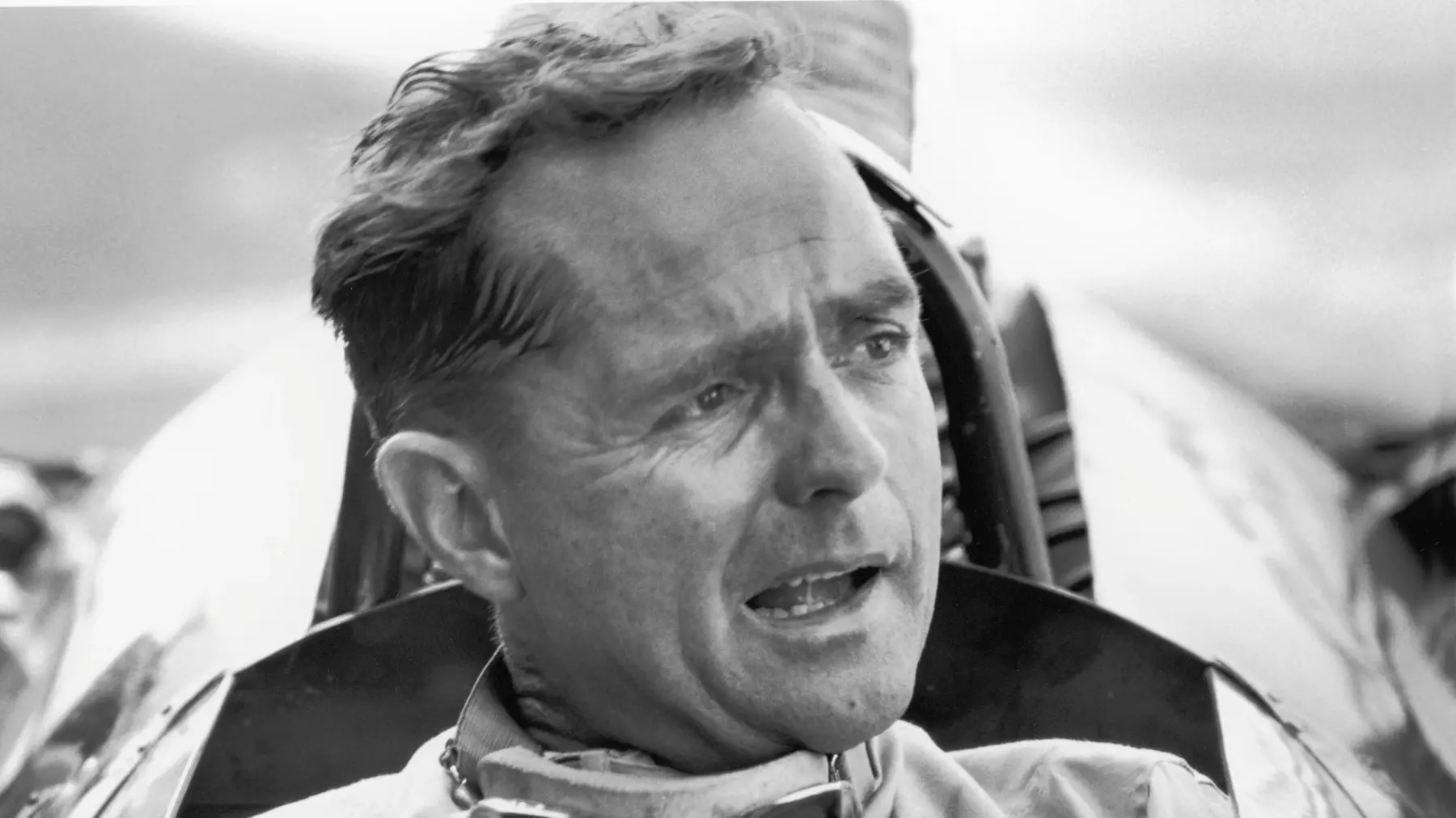 American Grand Prix racing car driver Phil Hill sits in his car and talks to the out-of-frame pit